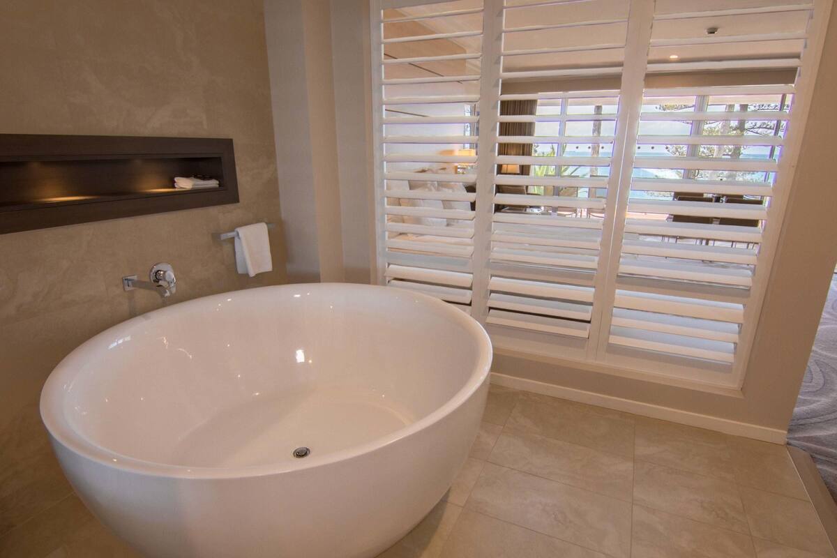 Un baño moderno con una bañera independiente, un perchero y una ventana con persianas.