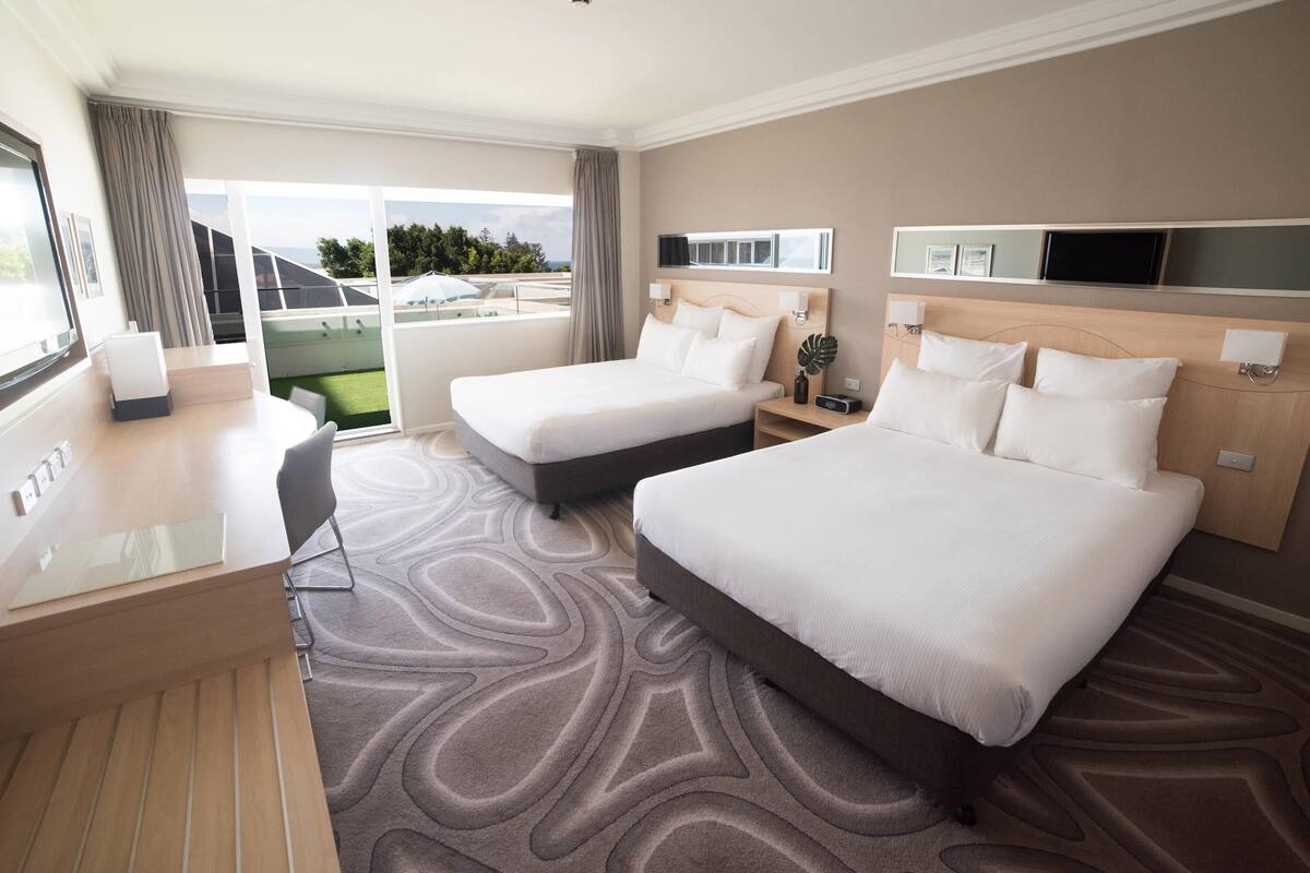 Habitación de hotel con dos camas, un escritorio, una silla, un televisor y vistas al exterior.