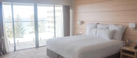 Une chambre d’hôtel avec un grand lit, une tête de lit en bois, une table de chevet et une vue sur la ville grâce à de grandes fenêtres.