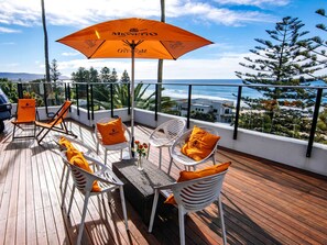 A deck with outdoor seating, a table, and a view of the ocean. - Novotel Wollongong Northbeach (North Wollongong)