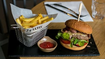 En burger med bolle, salat, tomat og ost, serveret med pommes frites og en lille skål ketchup.