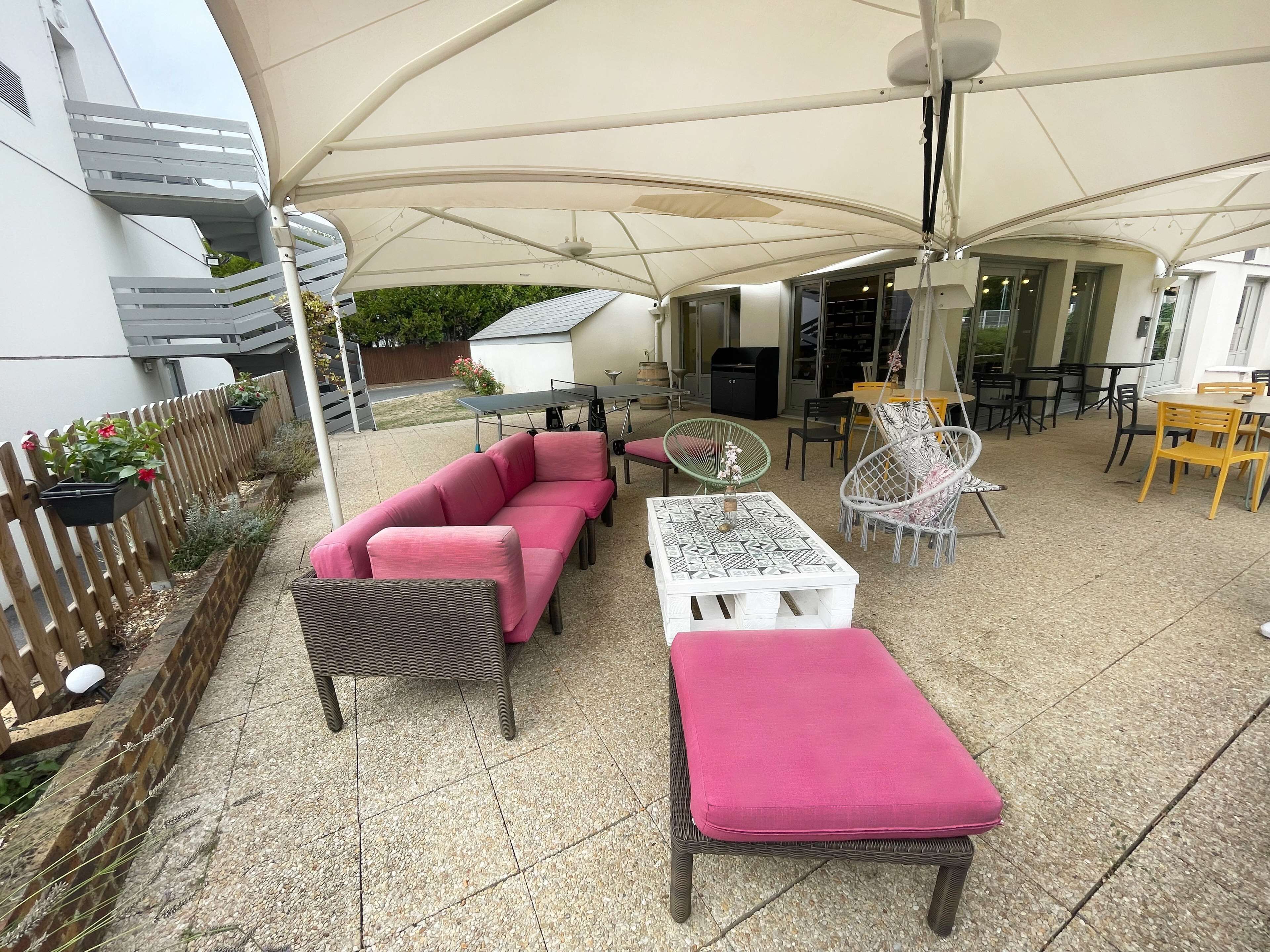 Un patio al aire libre con una zona de estar cubierta, una mesa de comedor y una parrilla.