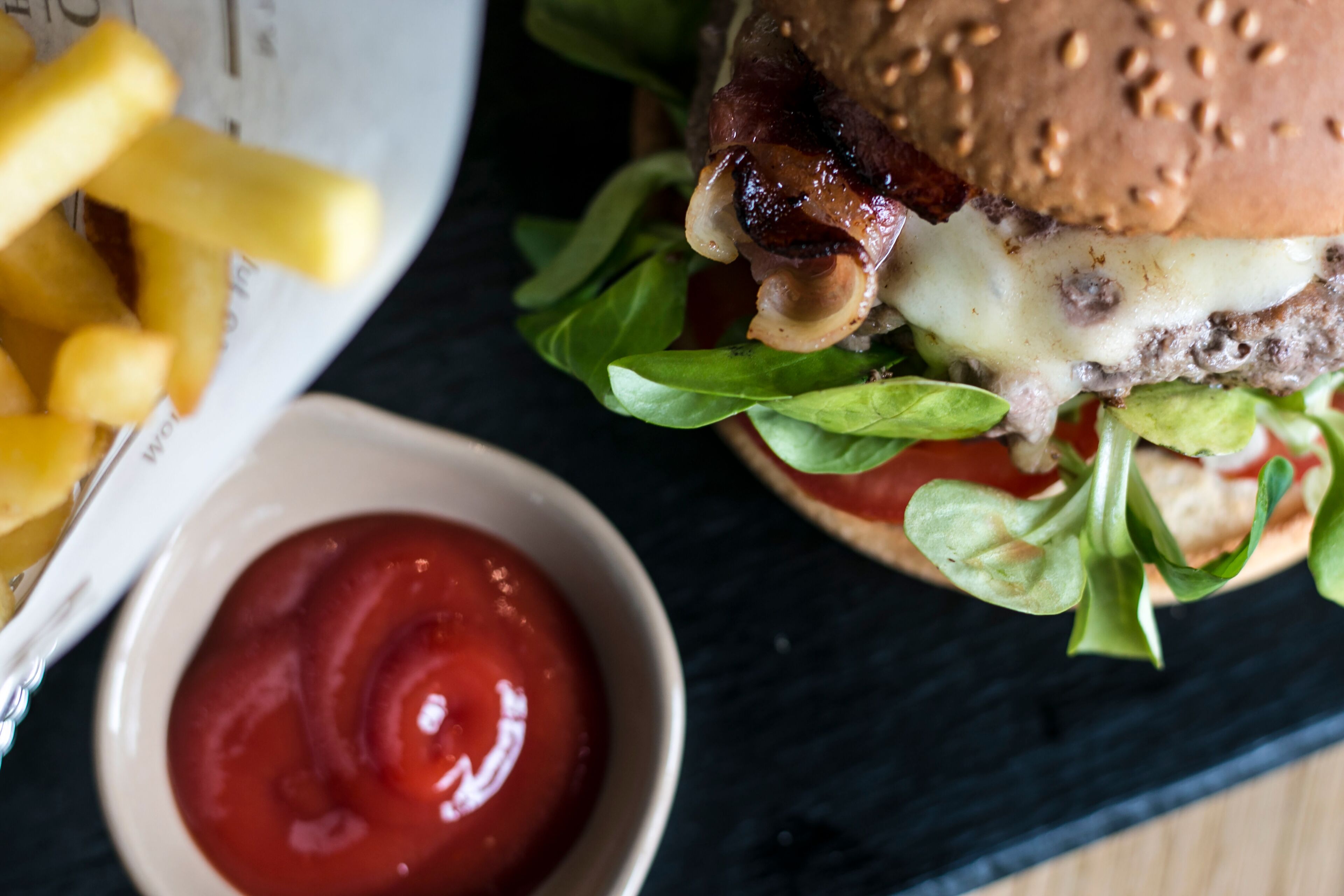 A burger with lettuce, cheese, and a sauce container.