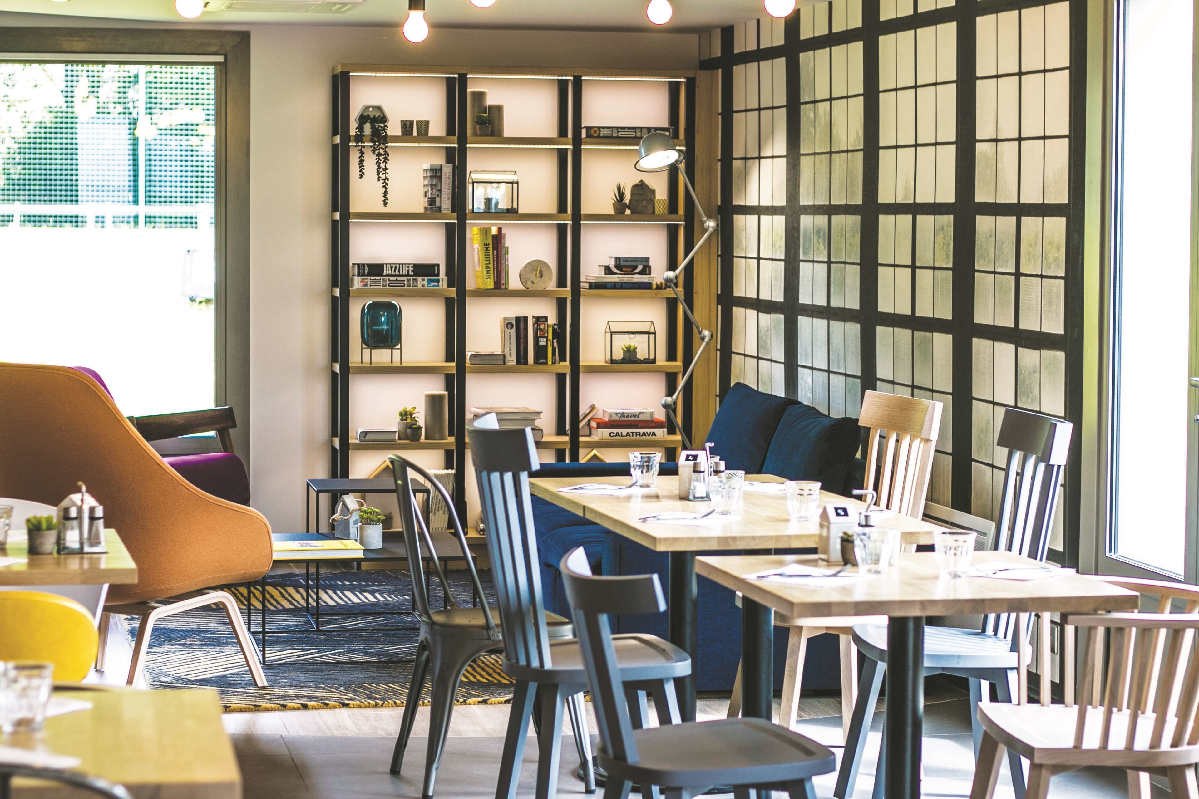 A cozy cafe with a wooden bookshelf, comfortable seating, and a large window.