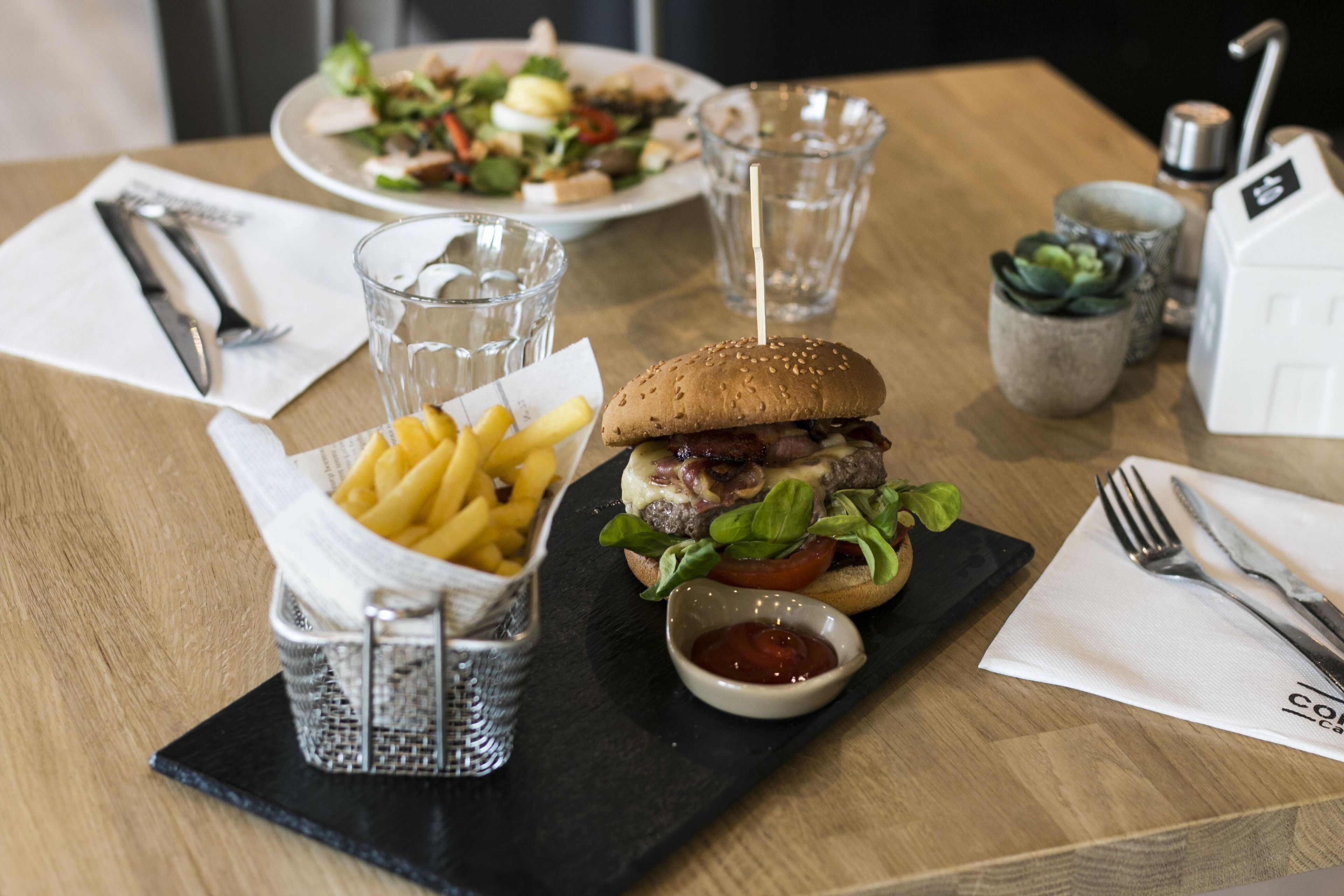 A meal consisting of a burger, fries, and a salad on a wooden table.