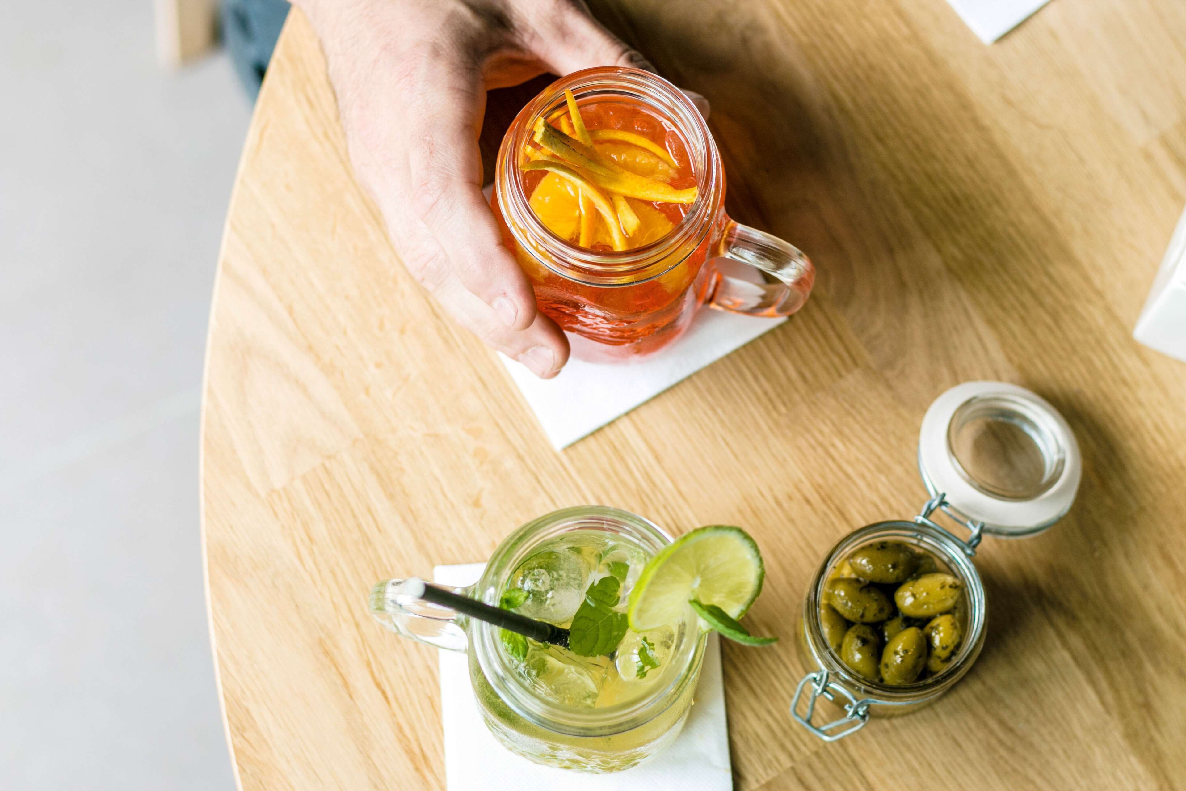 A hand holding a glass mug with a slice of orange and mint leaves.