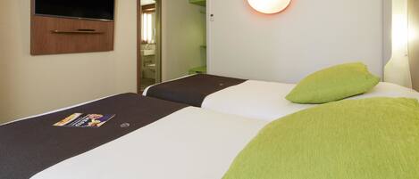 Habitación de hotel con dos camas, un televisor montado en la pared, una lámpara de noche y un almohadón verde en una de las camas.
