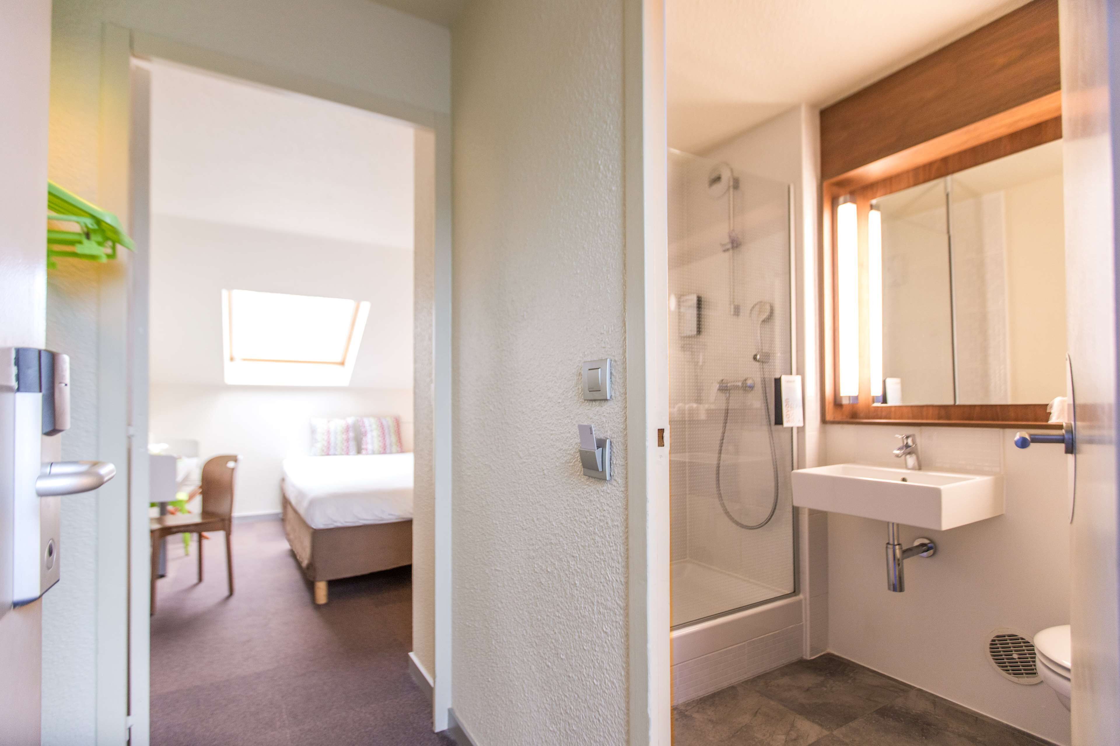 A hotel room with a bed, a desk, a chair, a shower, and a sink.