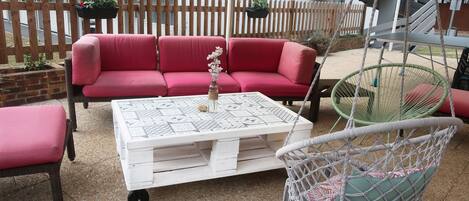 Un espace extérieur avec des sièges rouges, une table basse blanche et un fauteuil en macramé.