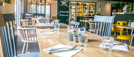 A restaurant with wooden tables and chairs, a chalkboard menu, and a bar area.