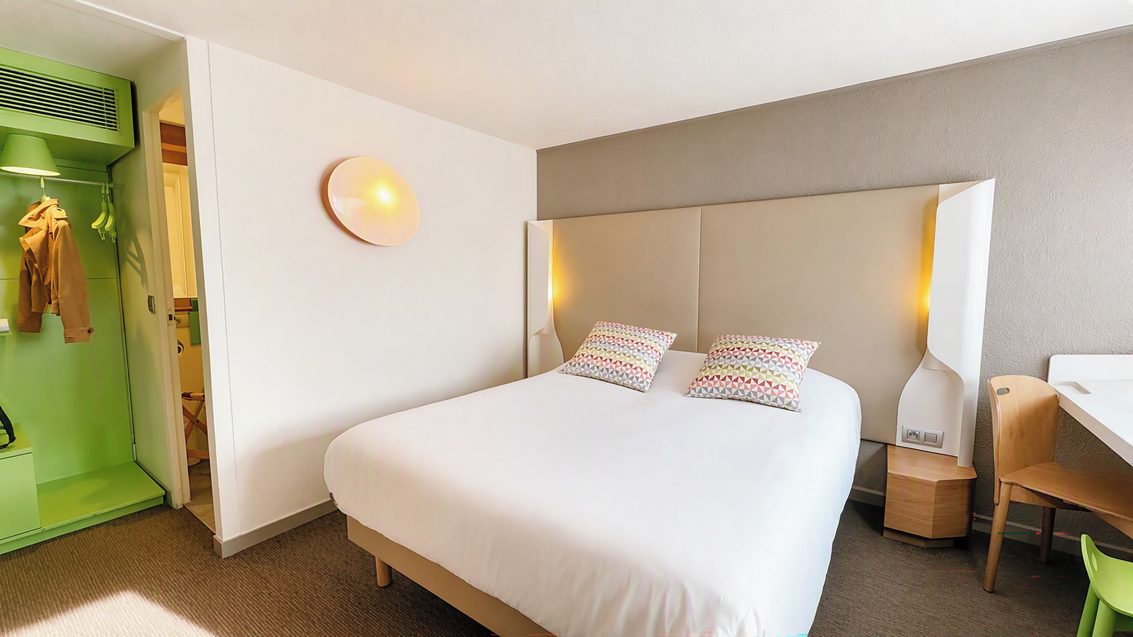 Una habitación de hotel con una cama, mesita de noche, lámpara y un armario verde.