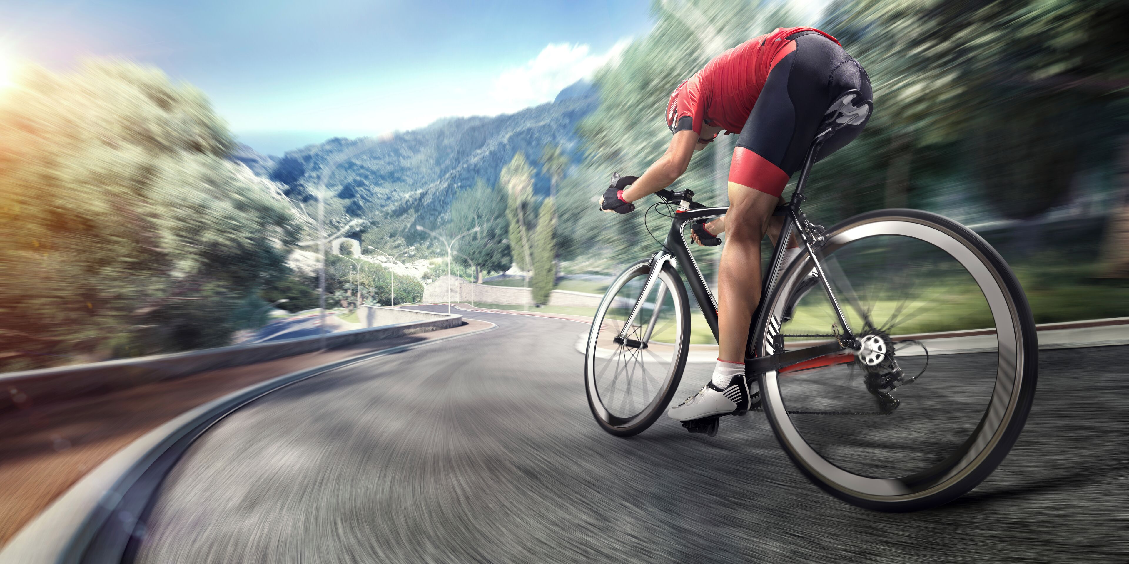A cyclist riding a road bike on a curved road with a mountainous landscape in the background.