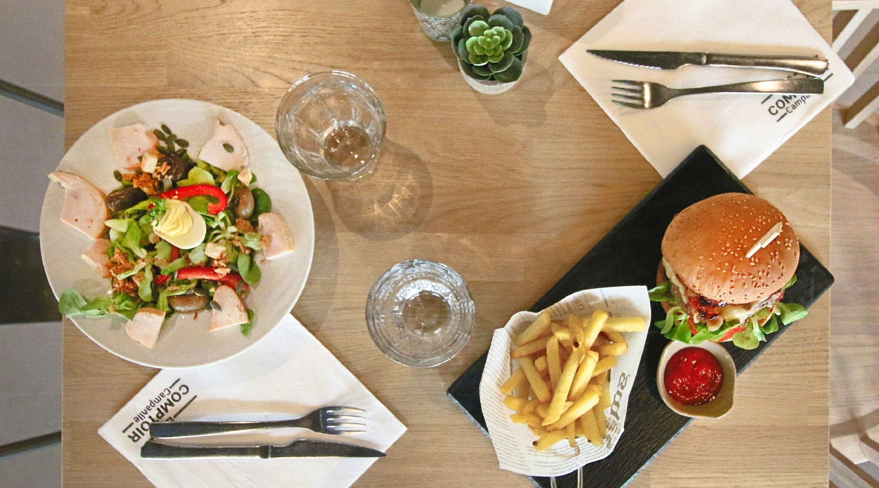 Un plato con ensalada, hamburguesa, papas fritas y una bebida sobre una mesa de madera.