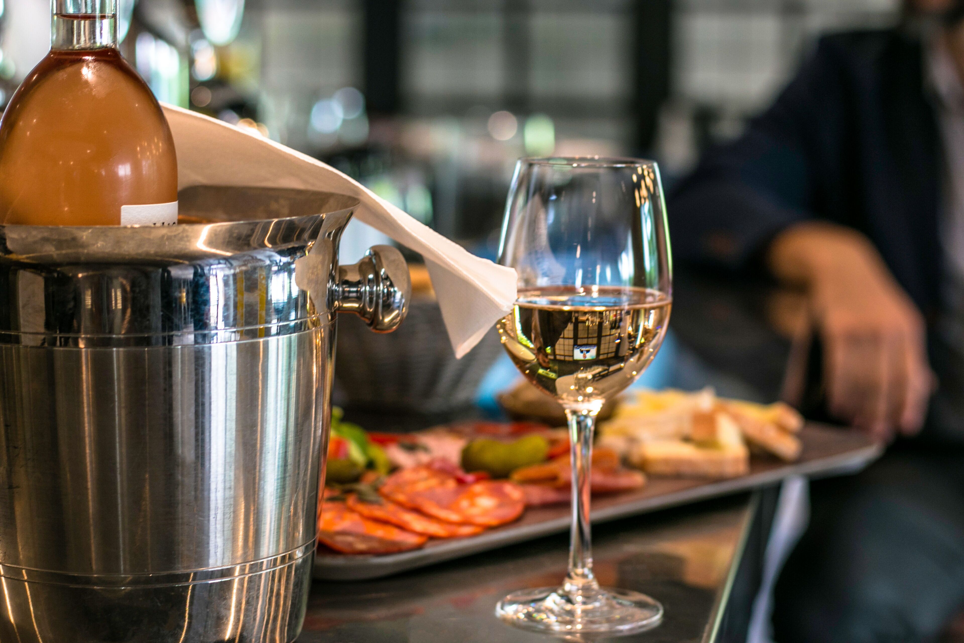 Un shaker de cócteles con una botella y una copa de vino blanco sobre una bandeja con comida.