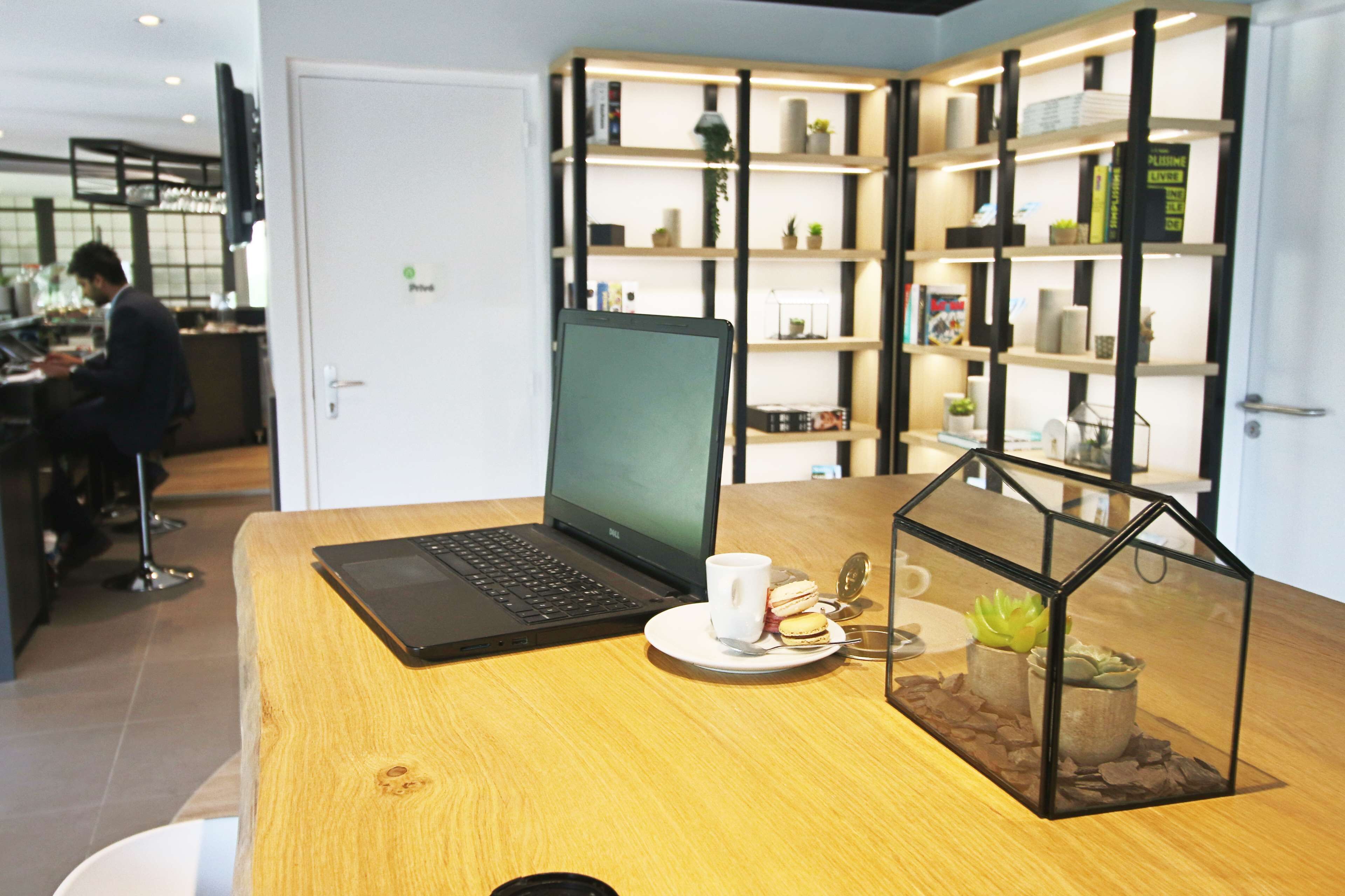 A wooden table with a laptop, a cup, and a glass terrarium.