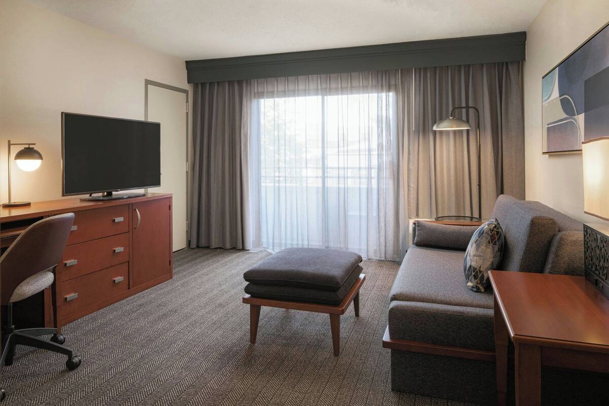 Een hotelkamer met een flatscreen televisie, een houten bureau, een comfortabele bank, een sofa en een lamp.