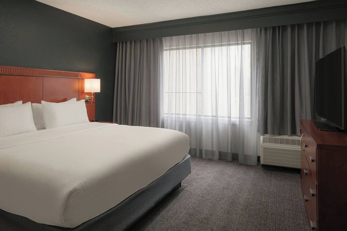 Hotelkamer met groot bed, flatscreen-tv, nachtkastje met lamp en raam met gordijnen.