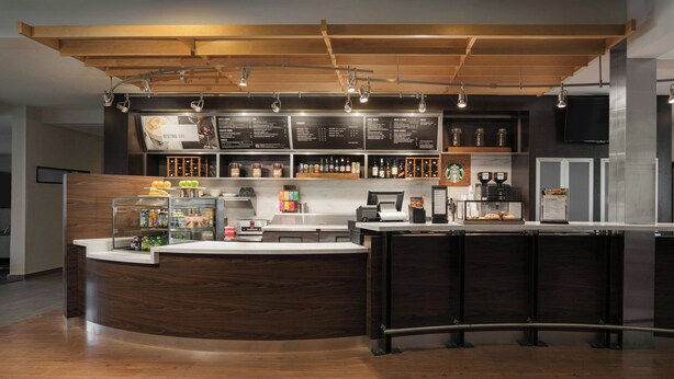 A modern bar area with a wooden counter, a menu board, and various bottles and glasses.