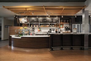 Een moderne bar met een houten toonbank, een menubord en verschillende flessen en glazen.