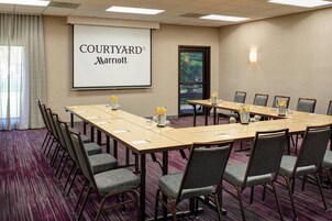A conference room with a long table, multiple chairs, a projector screen displaying 'COURTYARD Marriott', and a window with a view of trees.