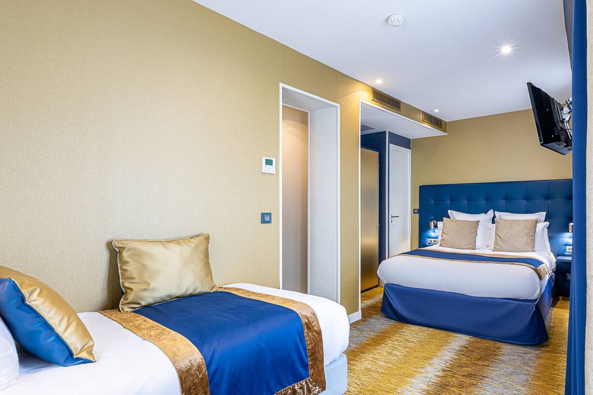 A hotel room with two beds, a TV mounted on the wall, and a door leading to another room.