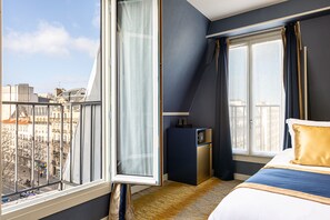 A hotel room with a large window, a bed, a desk, and a view of the city. - Trianon Gare de Lyon (Paris)