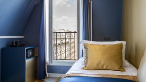 A hotel room with a bed, a desk, and a window with a view of buildings. - Trianon Gare de Lyon (Paris)