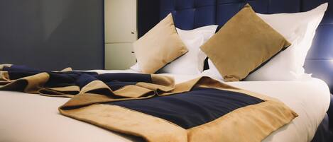 A neatly made bed with a blue headboard, multiple pillows, and a beige and navy throw blanket.