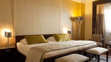 Quarto de hotel com uma cama grande, duas luminárias de cabeceira, uma cadeira e uma mesa pequena.