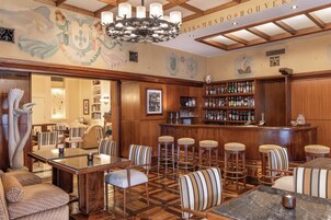 A bar area with wooden furniture, a chandelier, and a wall with coats of arms.