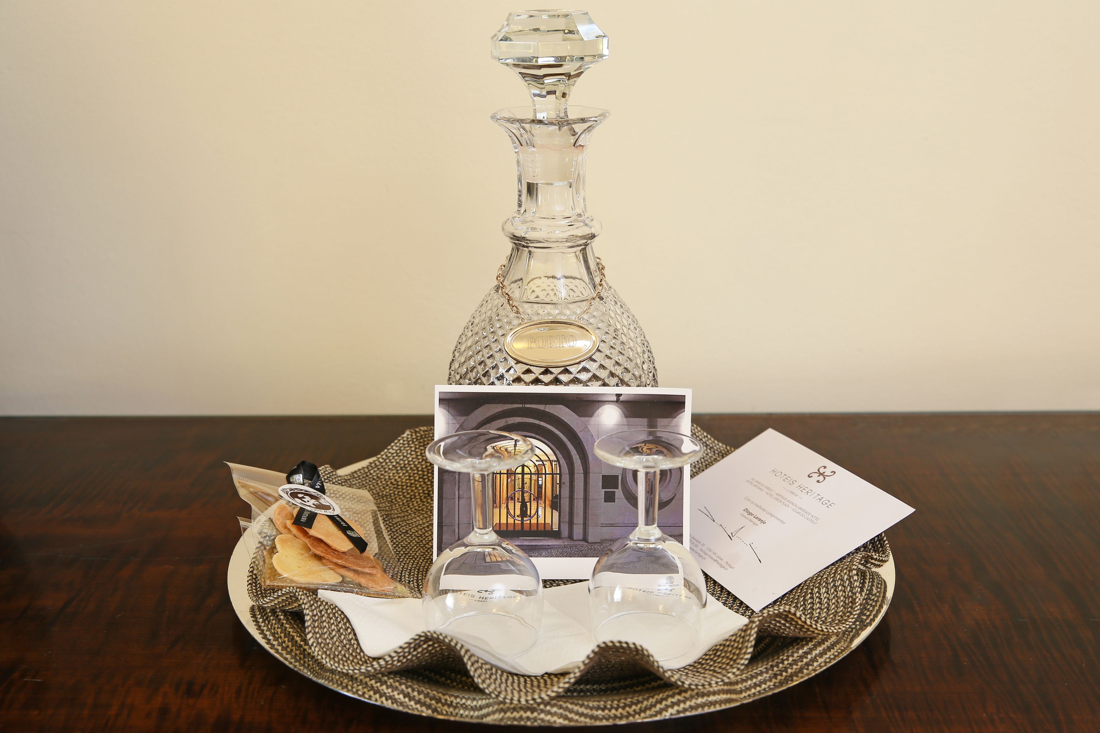 A crystal decanter, two wine glasses, a box, and a card on a woven tray.