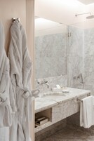 A modern bathroom with a marble sink, a towel rack, and a shower area.