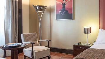 A hotel room with a bed, a chair, a lamp, a nightstand, a rug, and a painting on the wall.
