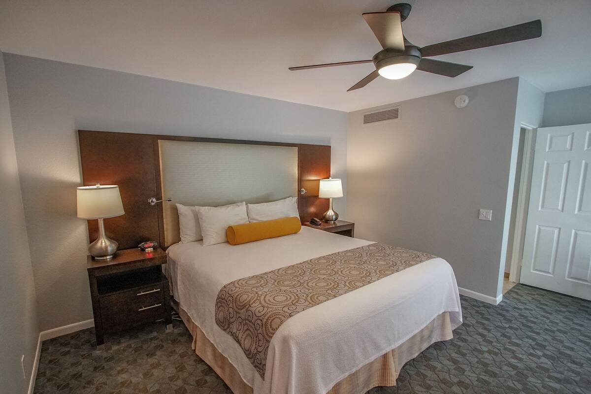 A hotel room with a large bed, two bedside tables with lamps, a ceiling fan, and a door.