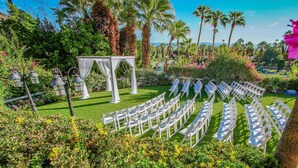 A garden venue with white chairs arranged in rows, a white gazebo, and palm trees. - Palm Springs Tennis Club (Palm Springs)