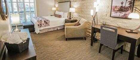 A hotel room with a bed, a chair, a desk, and a large window.