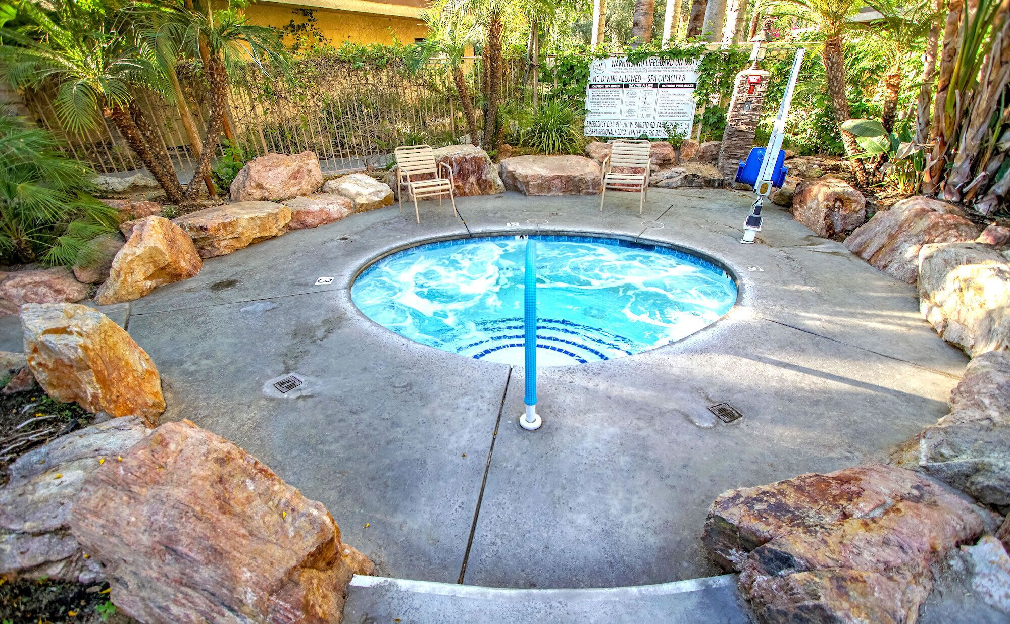A circular hot tub surrounded by rocks and plants, with a sign indicating no diving allowed and spa capacity.
