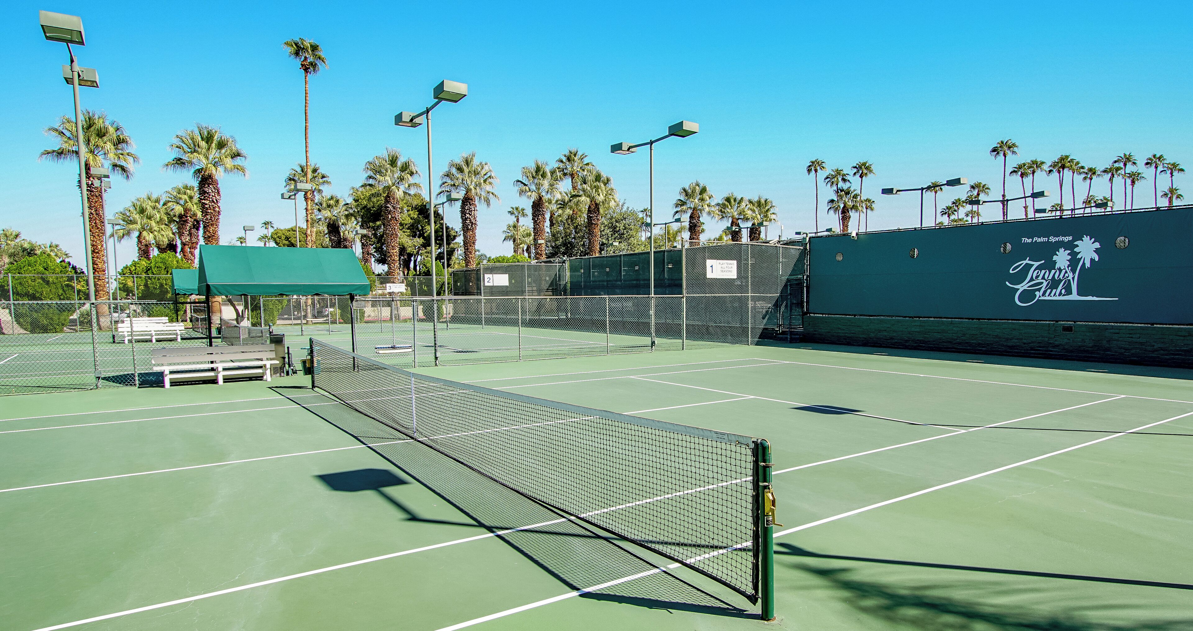 A tennis court with a net, benches, and a fence.