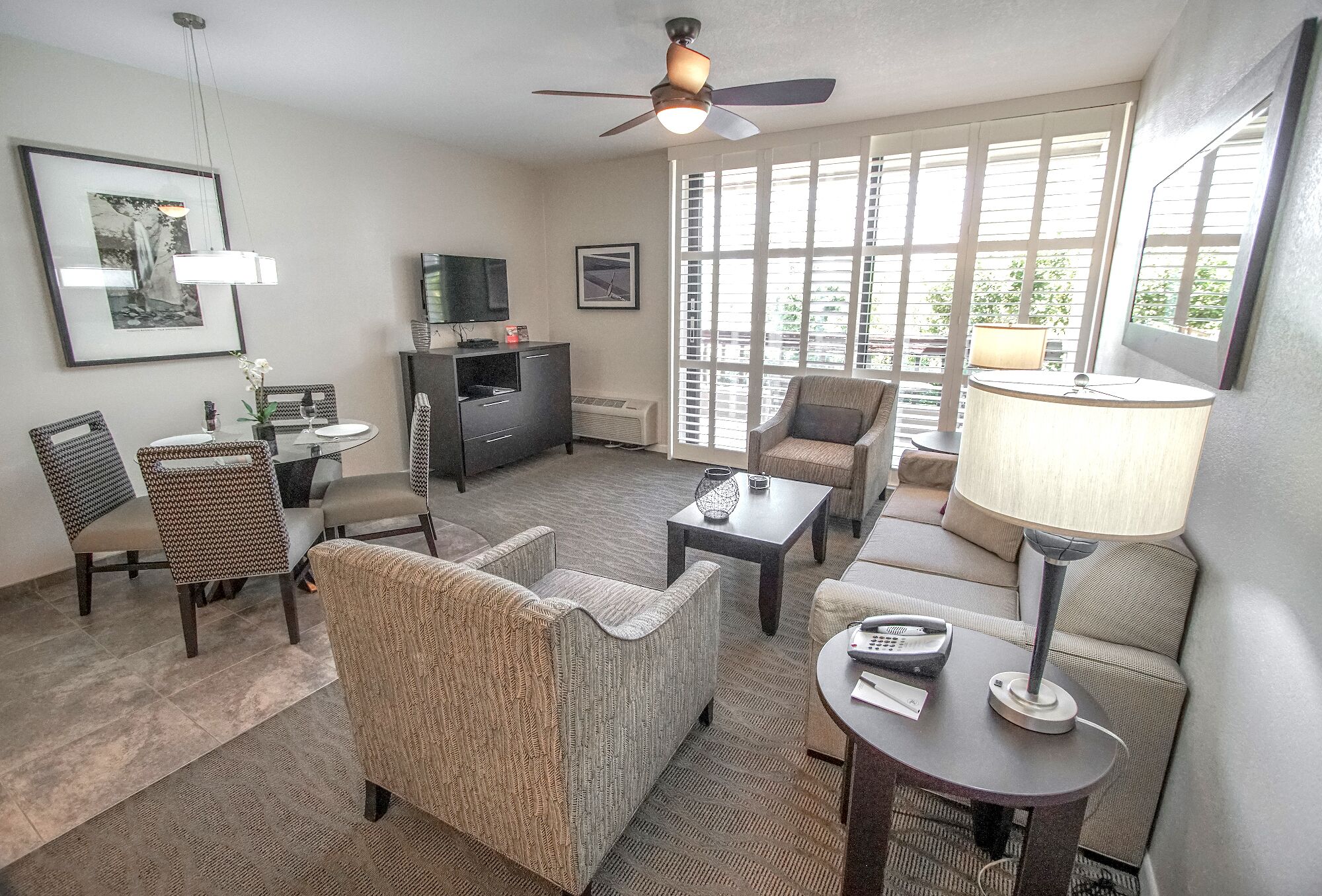 A living room with a ceiling fan, a dining table with chairs, a sofa, a TV, and a window with blinds.