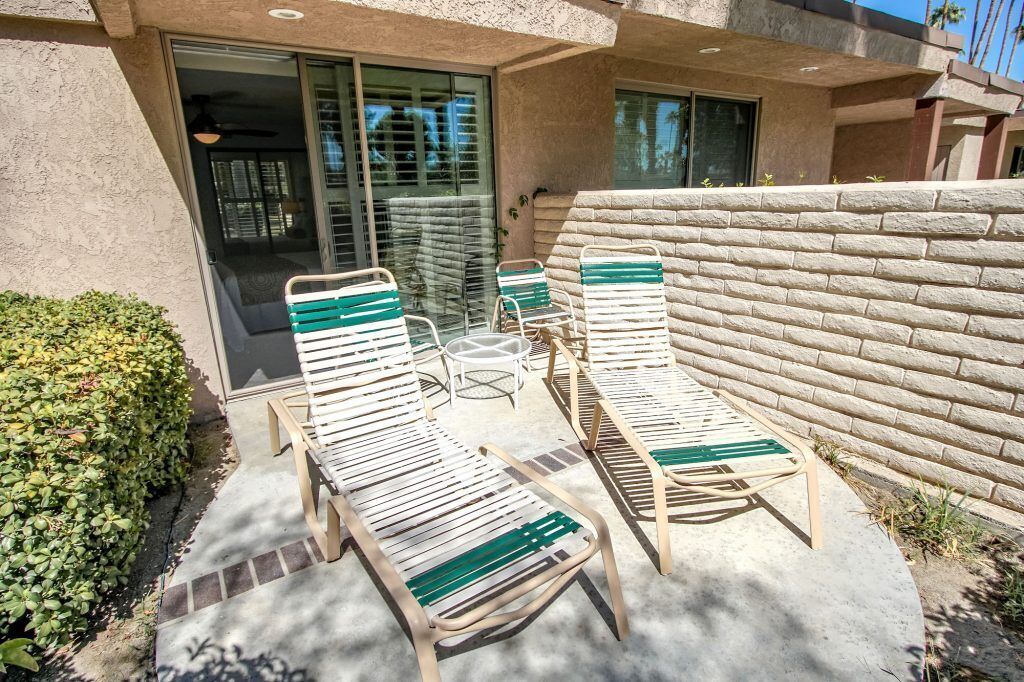 Een terras met vier loungesteilen en een tafel, een stenen muur en een glazen deur die naar een binnenruimte leidt.