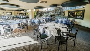 A spacious dining area with round tables set for a meal, large windows, and a rock wall feature. - Palm Springs Tennis Club (Palm Springs)