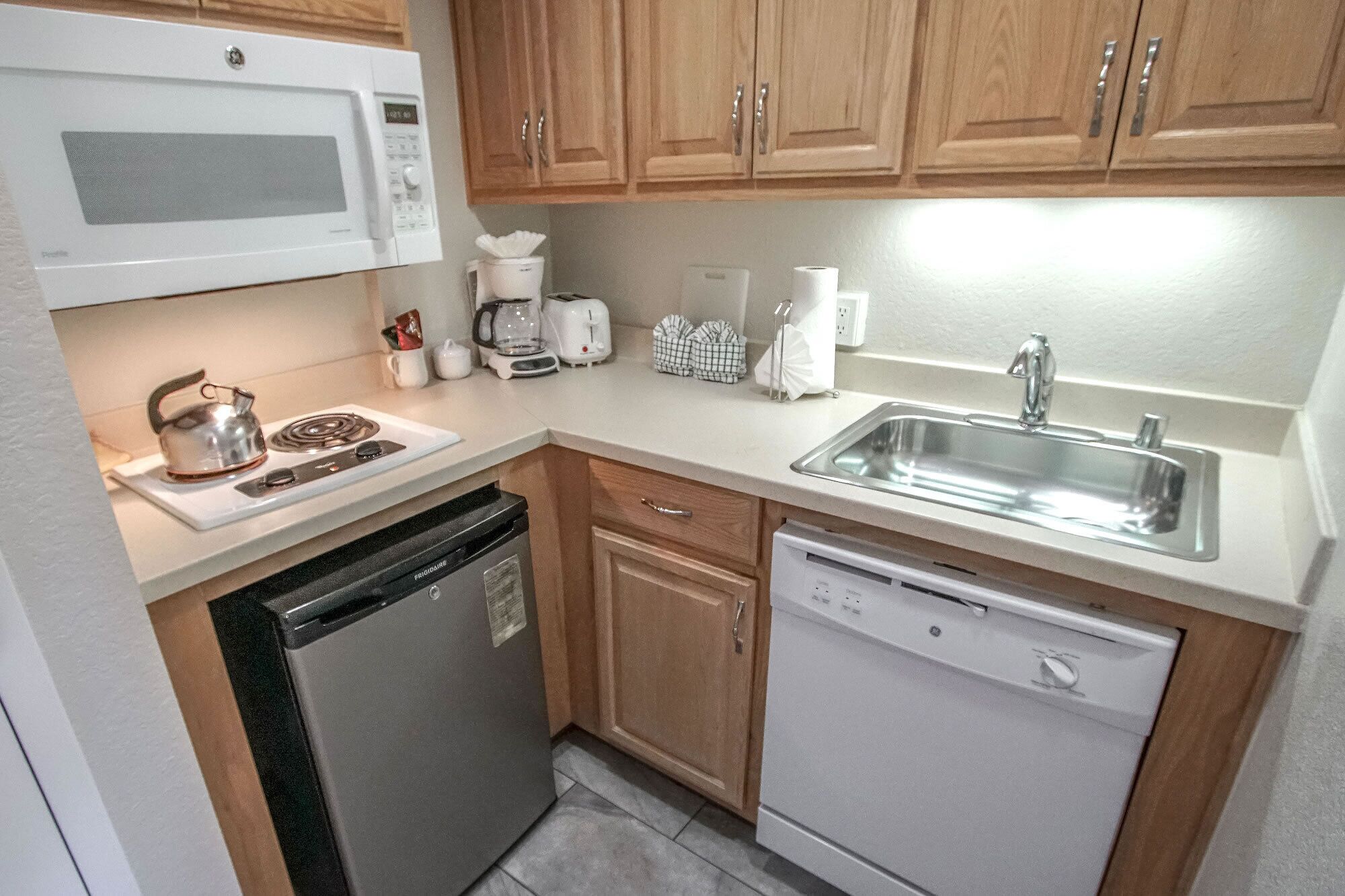 A compact kitchen with a microwave, kettle, coffee maker, toaster, and dishwasher.