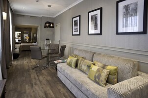 A hotel room with a patterned sofa, a dining table with chairs, and framed pictures on the wall.