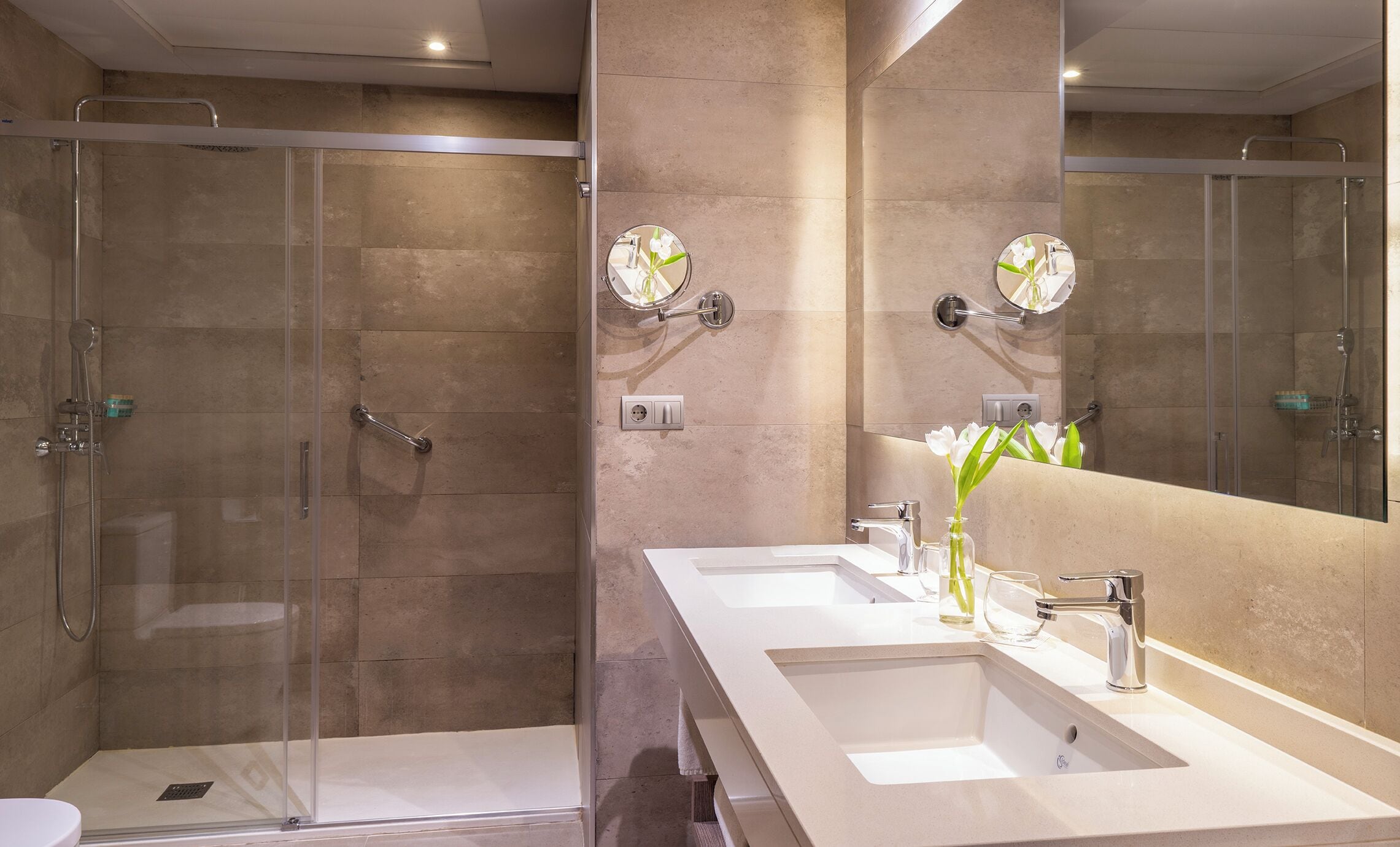 Une salle de bain moderne avec une douche à parois de verre, un grand miroir et deux lavabos.
