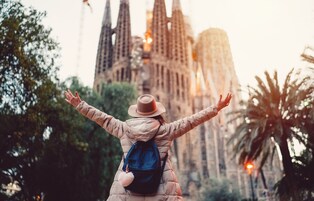 Uma pessoa de braços abertos, olhando para uma grande catedral com várias torres.