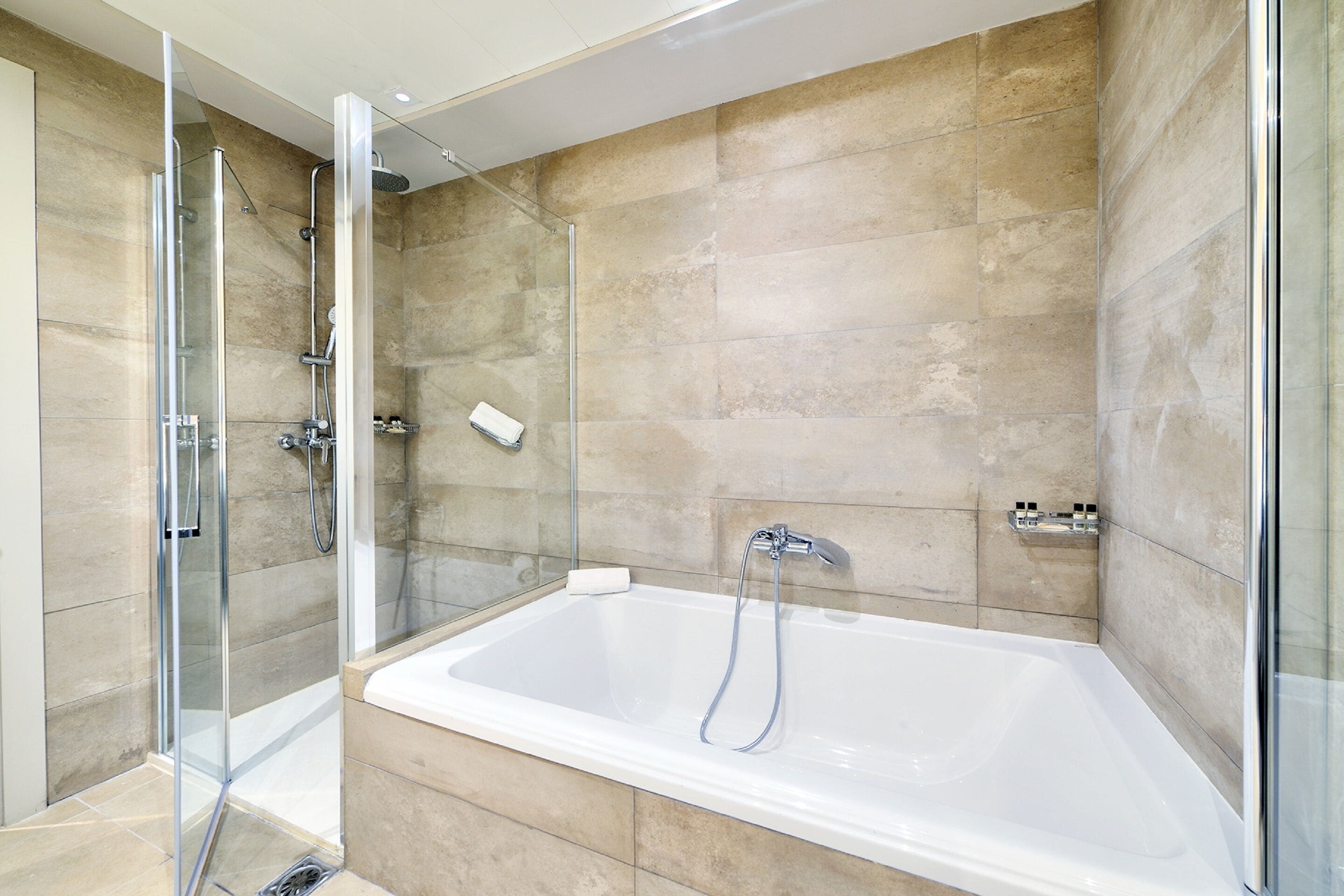 A modern bathroom with a glass-enclosed shower, a large bathtub, and beige tiled walls.
