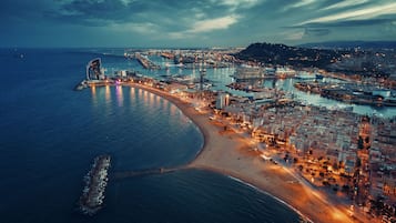 An aerial view of a coastal city with a prominent curved building, a beach, and a marina.