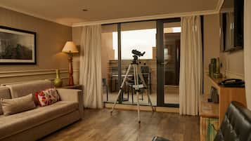 Habitación de hotel con sofá, un trípode y zona de comedor visibles a través de puertas de vidrio.