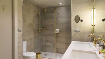 A modern bathroom with a glass-enclosed shower, a white toilet, and a double sink with gold fixtures.