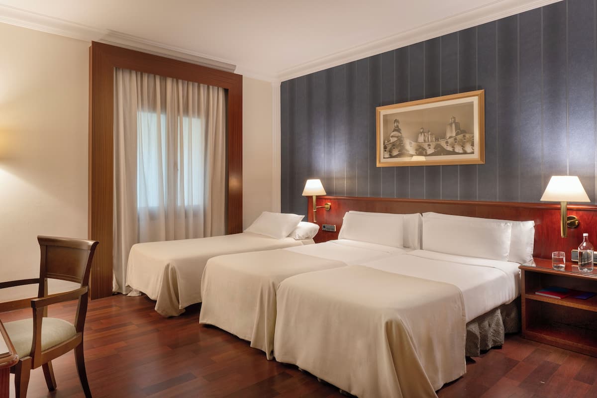 Une chambre d’hôtel avec deux lits, un bureau, une chaise, une table de chevet et un tableau au mur.